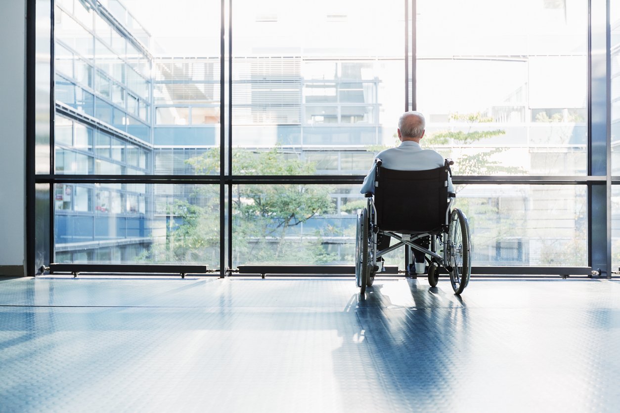 Senior Man in Wheelchair Elderly nursing home resident sitting alone in wheelchair near window representing isolation and signs of nursing home neglect.