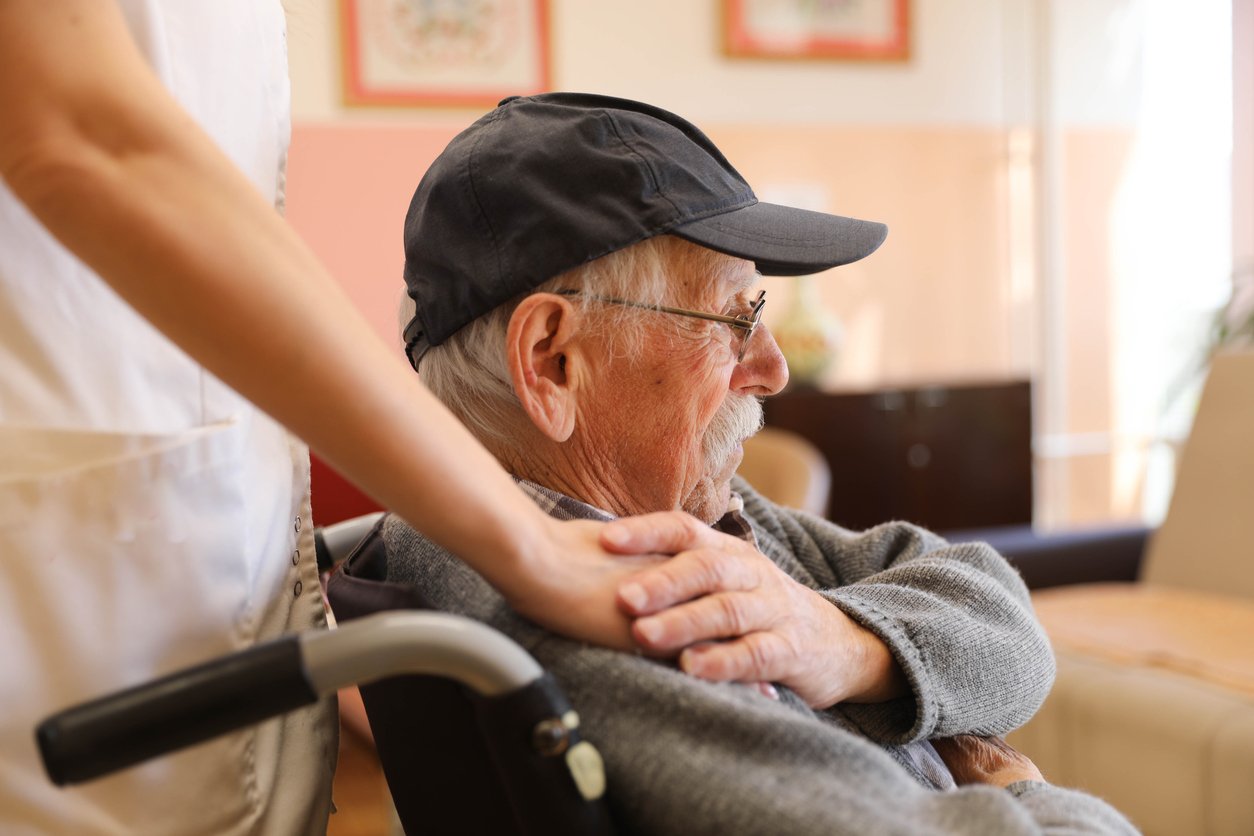 Elderly Man in a Wheelchair Talking to a Nurse at a Nursing Home Caregiver supporting elderly man in wheelchair at nursing home facility to represent elder care and abuse prevention.